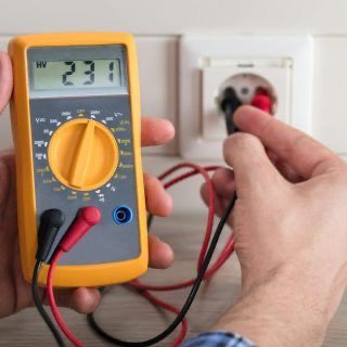 Elektriker misst mit einem digitalen Multimeter die Spannung an einer Steckdose.