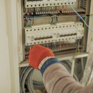 Hand eines Elektrikers arbeitet an einem geöffneten Sicherungskasten mit Schaltmodulen.