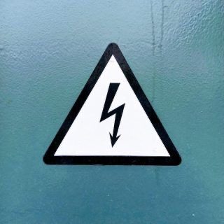 Warnschild mit Blitzsymbol weist auf elektrische Spannung und Stromschlaggefahr hin.