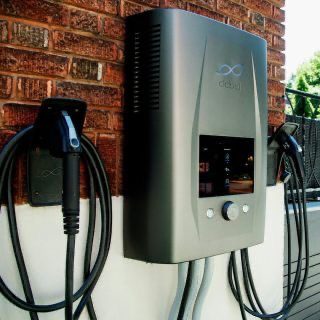 Wallbox mit angeschlossenem Ladekabel für Elektrofahrzeuge an einer Hauswand.